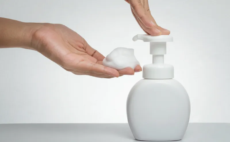 Photo of a bottle of hand soap and a hand catching the bubbles coming out of it. Liquid soap is being turned into foam through the mesh filter.