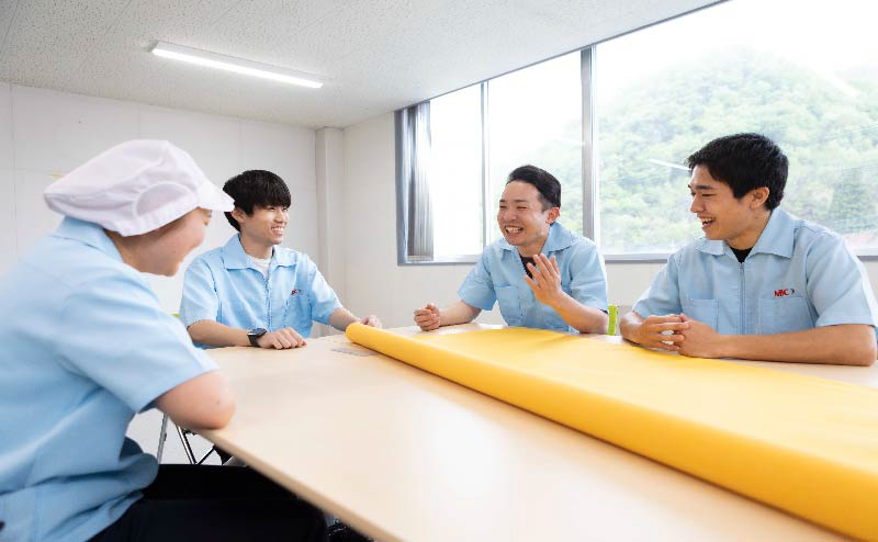 Workers discussing around a yellow screen printing mesh roll in a meeting room